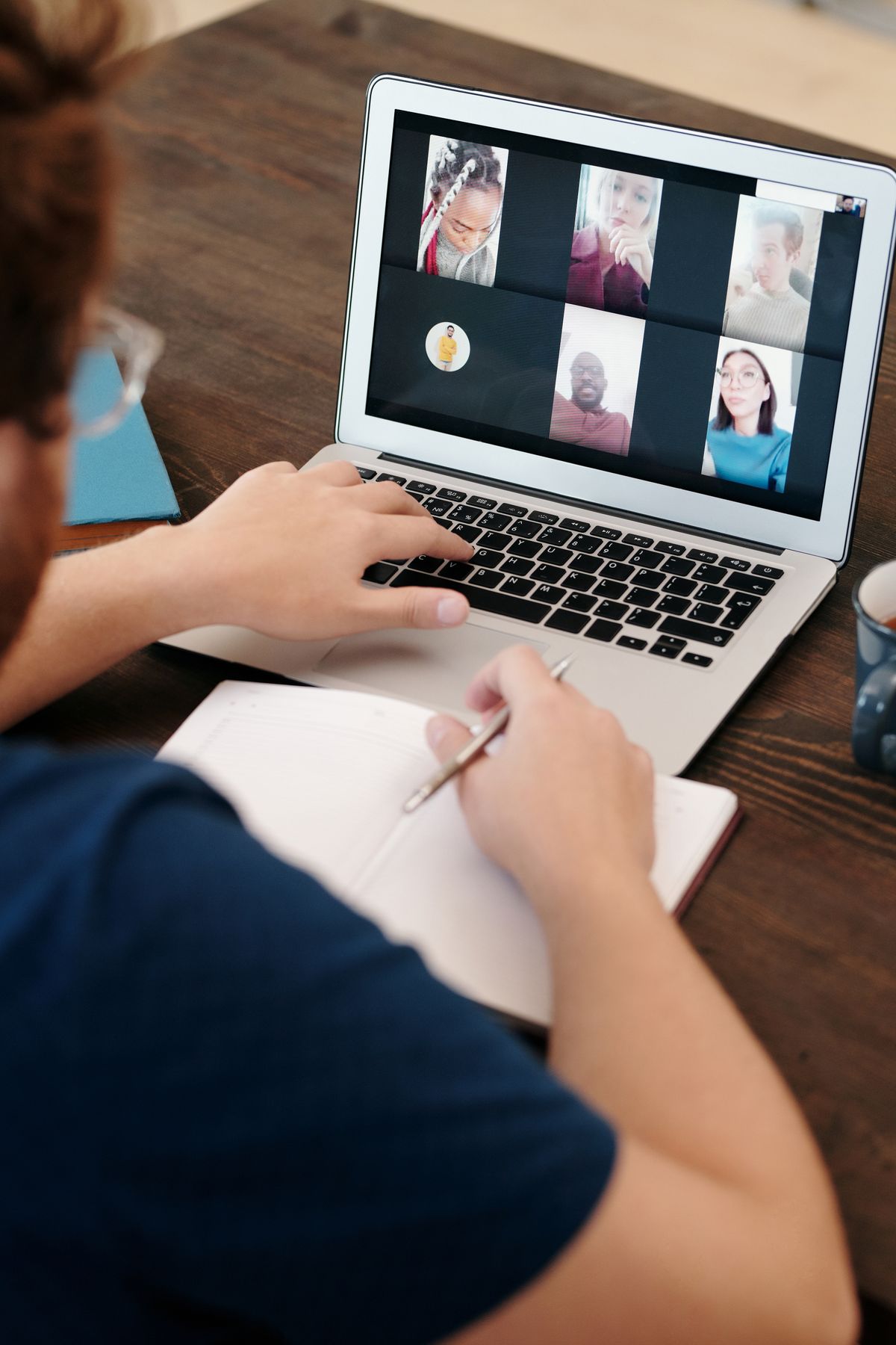 Persoon maakt aantekeningen tijdens een online vergadering met een divers team op het laptopscherm